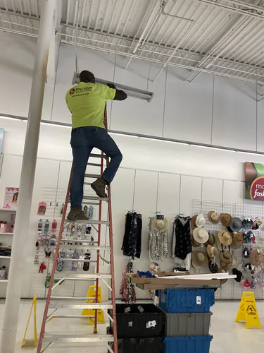 Spectrum Electric technician on a ladder installing a linear LED strip fixture above the Bealls sales floor
