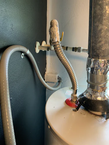 Flexible metal conduit whip strapped to the closet wall beside the water heater flue and cold water flex in Casselberry