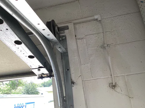 Schedule 40 PVC conduit strapped along a garage block wall above the door track and turning into a cored penetration in Longwood