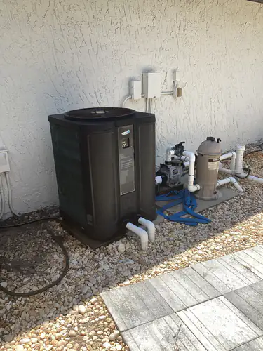 Pool heat pump, circulation pump and cartridge filter on the equipment pad with conduit and enclosures on the stucco wall in Longwood