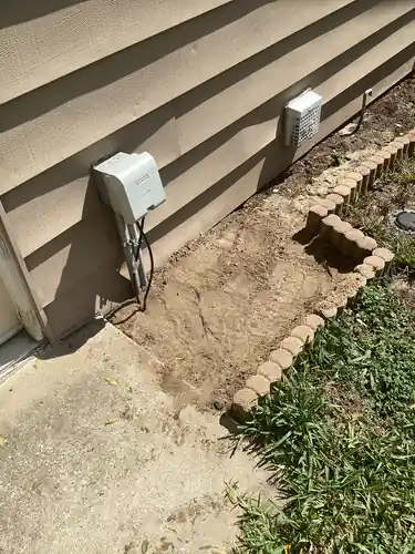 Weatherproof in use cover and conduit at the exterior wall of a Mount Dora home with the backfilled trench running out across the flower bed