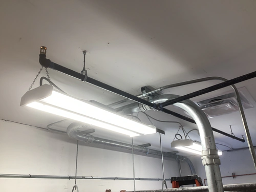Chain hung linear LED strip fixtures and galvanized conduit under the EMS warehouse roof