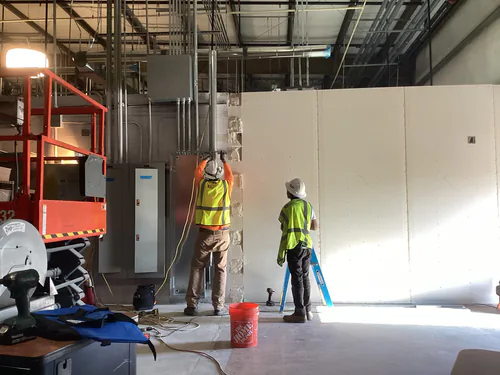 Two electricians running conduit from a panelboard up a block column inside the EMS warehouse