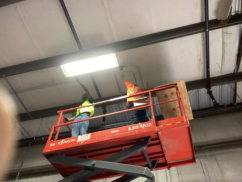 Electricians on a Skyjack lift installing a high bay fixture under the EMS warehouse roof deck