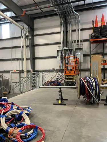 Conduit risers, wire reels and a JLG lift staged in the EMS warehouse before the feeder pull