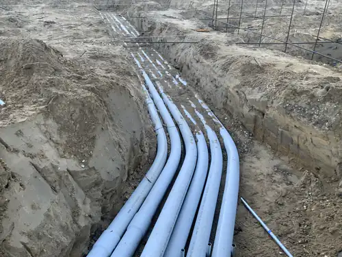 Bank of gray PVC conduits swept into a trench toward the Hawthorne Heights building