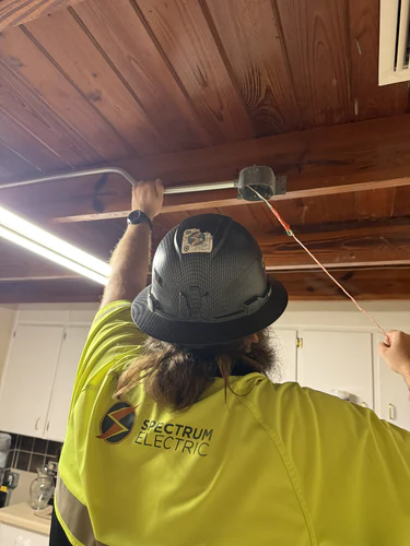 Electrician setting conduit into a new ceiling box in a wood plank ceiling in Winter Park