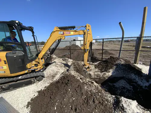 CAT excavator opening a conduit trench along the fence line at Massey Cadillac