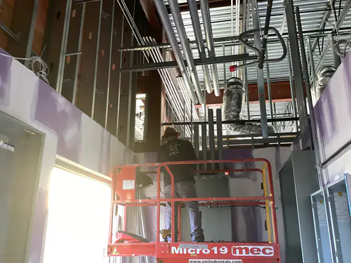 Electrician on a scissor lift running conduit high above the Massey Cadillac showroom