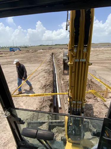 Electrician walking a trench line with gray PVC conduit laid in at the Massey Cadillac site