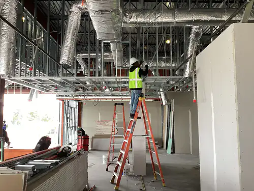 Electrician on a ladder working above the suspended ceiling grid during the Massey Cadillac build out in Orlando