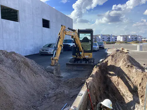 CAT mini excavator digging a conduit trench beside the tilt wall at Massey Cadillac