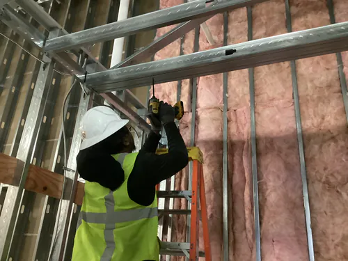 Electrician fastening metal stud framing above an insulated wall at Massey Cadillac