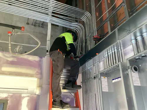 Electrician on a ladder terminating conduit into a wall mounted enclosure at Massey Cadillac