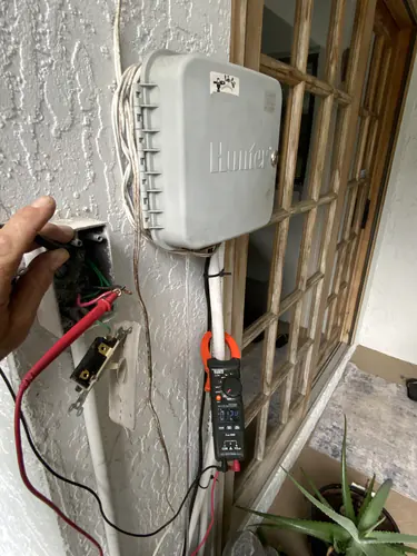 Klein clamp meter reading 124 volts at the replaced outdoor master switch beside a Hunter irrigation controller in Oviedo