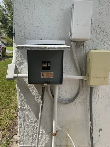 Gray metal breaker enclosure with a two pole breaker on the stucco side wall of an Oviedo home beside an Intermatic timer box