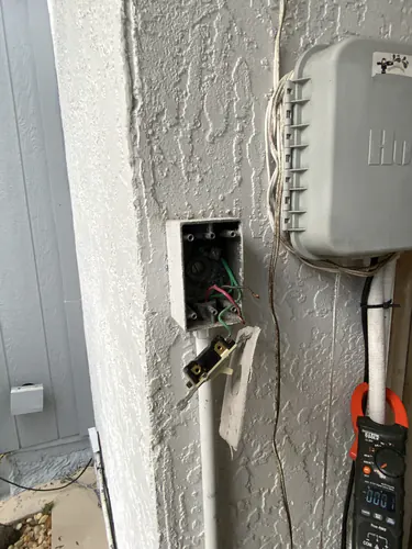 Outdoor switch box with the cover off showing red and black conductors and green grounds beside a Hunter controller in Oviedo