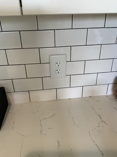 New 20 amp duplex receptacle and white cover plate set into the Oviedo kitchen backsplash above the countertop