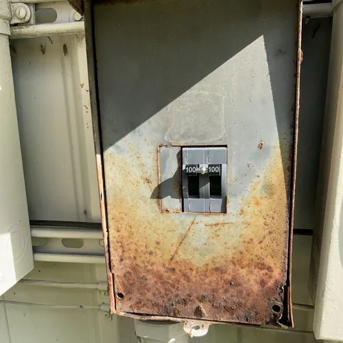 New two pole 100 amp main breaker showing through the original rusted enclosure cover in Orlando