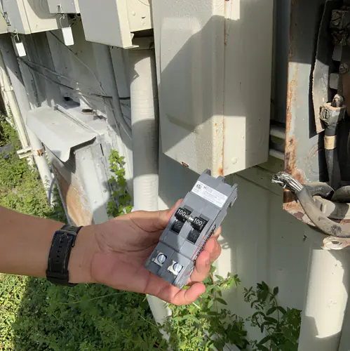 Electrician holding the new two pole 100 amp common trip breaker beside the open disconnect enclosure