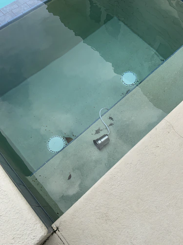 Stainless steel underwater pool light out of its niche and resting on a submerged step by its white cord at a Winter Park pool