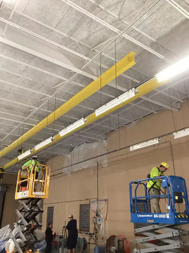 Two electricians on scissor lifts beside the monorail beam at the Hunter's Creek water facility