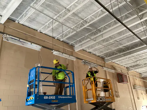 Electricians on two scissor lifts working overhead inside the Hunter's Creek water facility