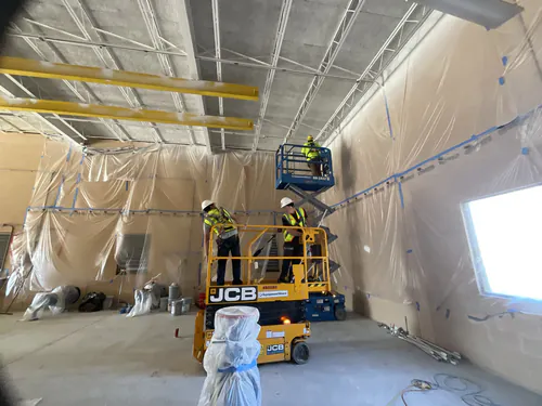 Two Spectrum Electric technicians on scissor lifts hanging strip lighting inside the Hunter's Creek water supply facility