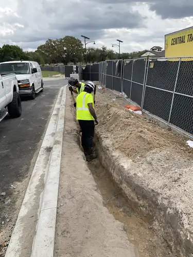 Electrician hand digging a conduit trench along the curb at the Lady Lake Market site