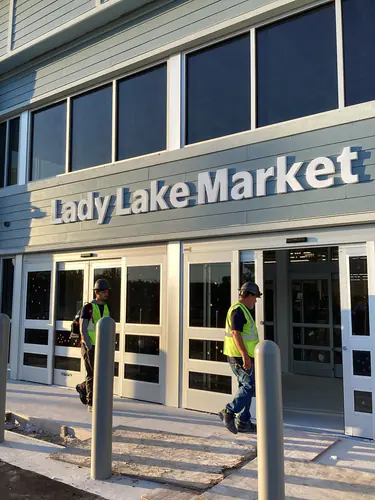 Two workers walking out of the Lady Lake Market entrance under the new storefront signage