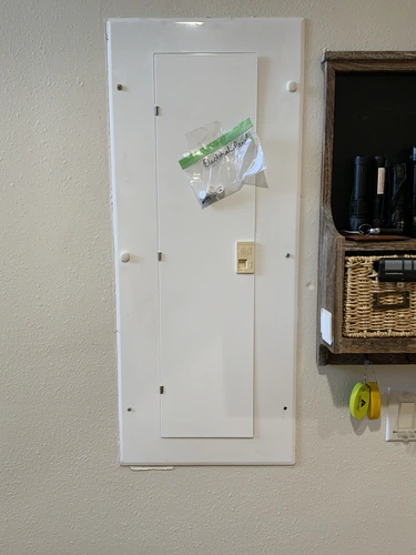 Flush mounted panel cover on a Winter Park wall with a bag of cover screws marked Electrical Panel taped to the door